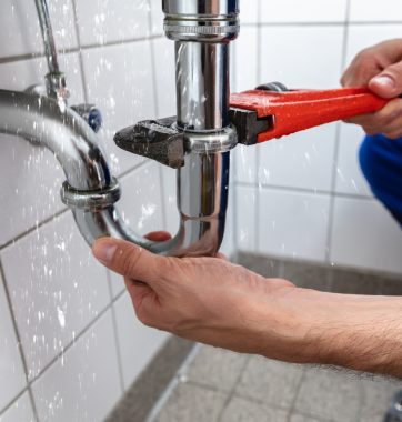 Male Plumber's Hand Repairing Sink Pipe Leakage With Adjustable Wrench